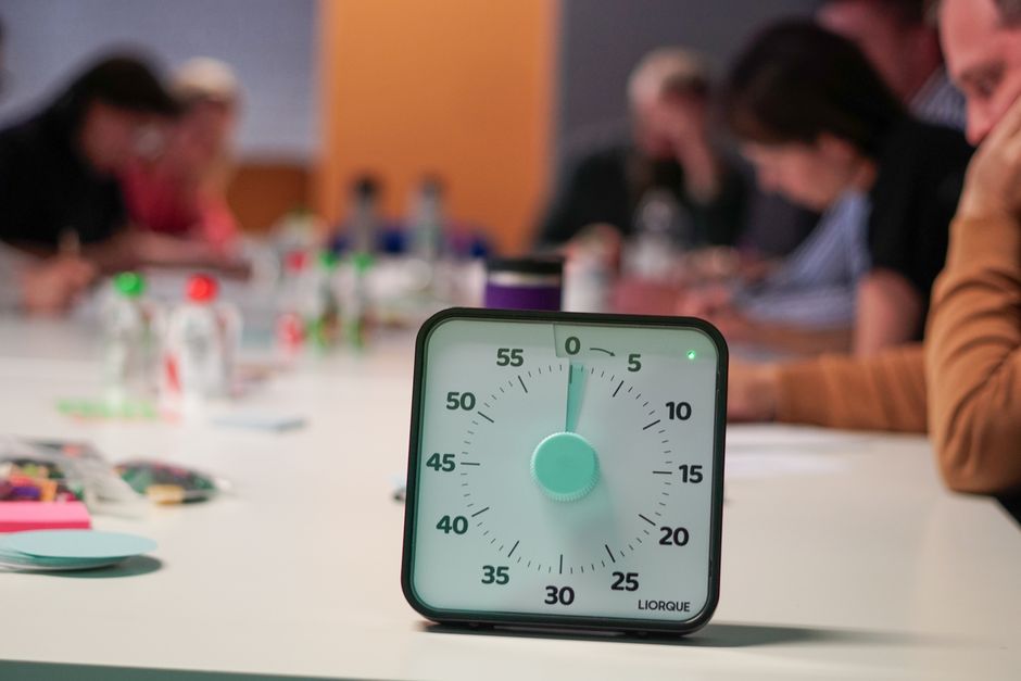 Timer on a table with blurred people in an office meeting setting, emphasizing focus.