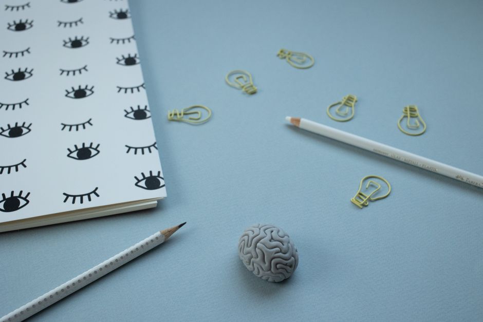 Artistic arrangement of pencils, notepad, brain model, and light bulb paperclips.